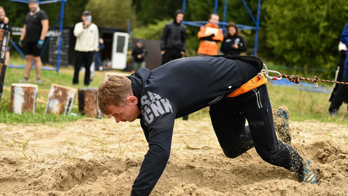 Man demonstrating strength as he crawls in a sand obstacle course with a body harness outdoors.
